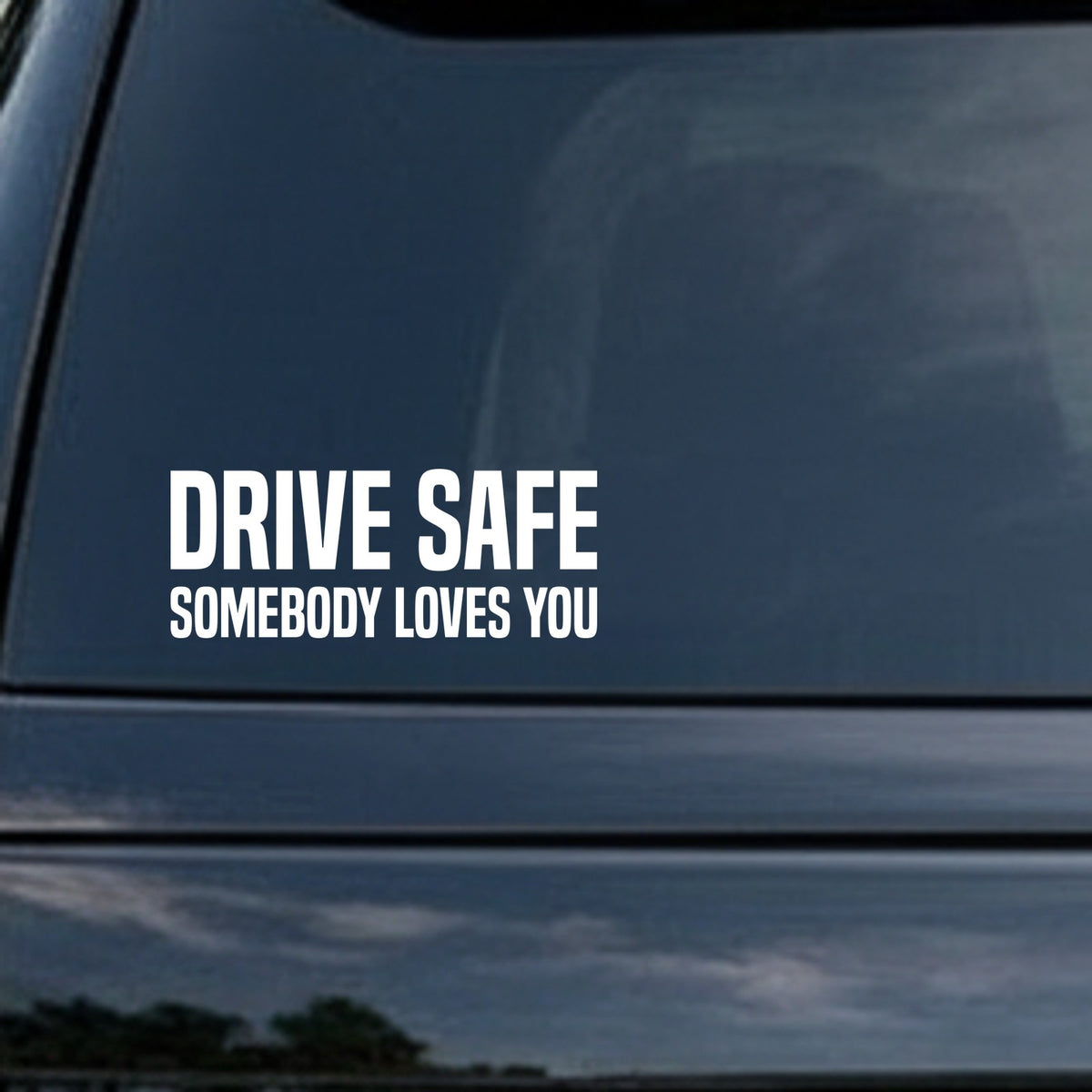 White vinyl decal with bold uppercase letters reading Drive Safe Somebody Loves You on a black background in a simple block style.