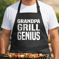 Black apron with large white bold slab font text reading Grandpa Grill Genius in three stacked rows