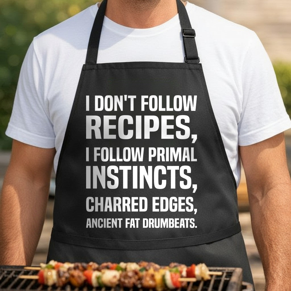 Black apron with large white text reading I Don’t Follow Recipes I Follow Primal Instincts Charred Edges Ancient Fat Drumbeats