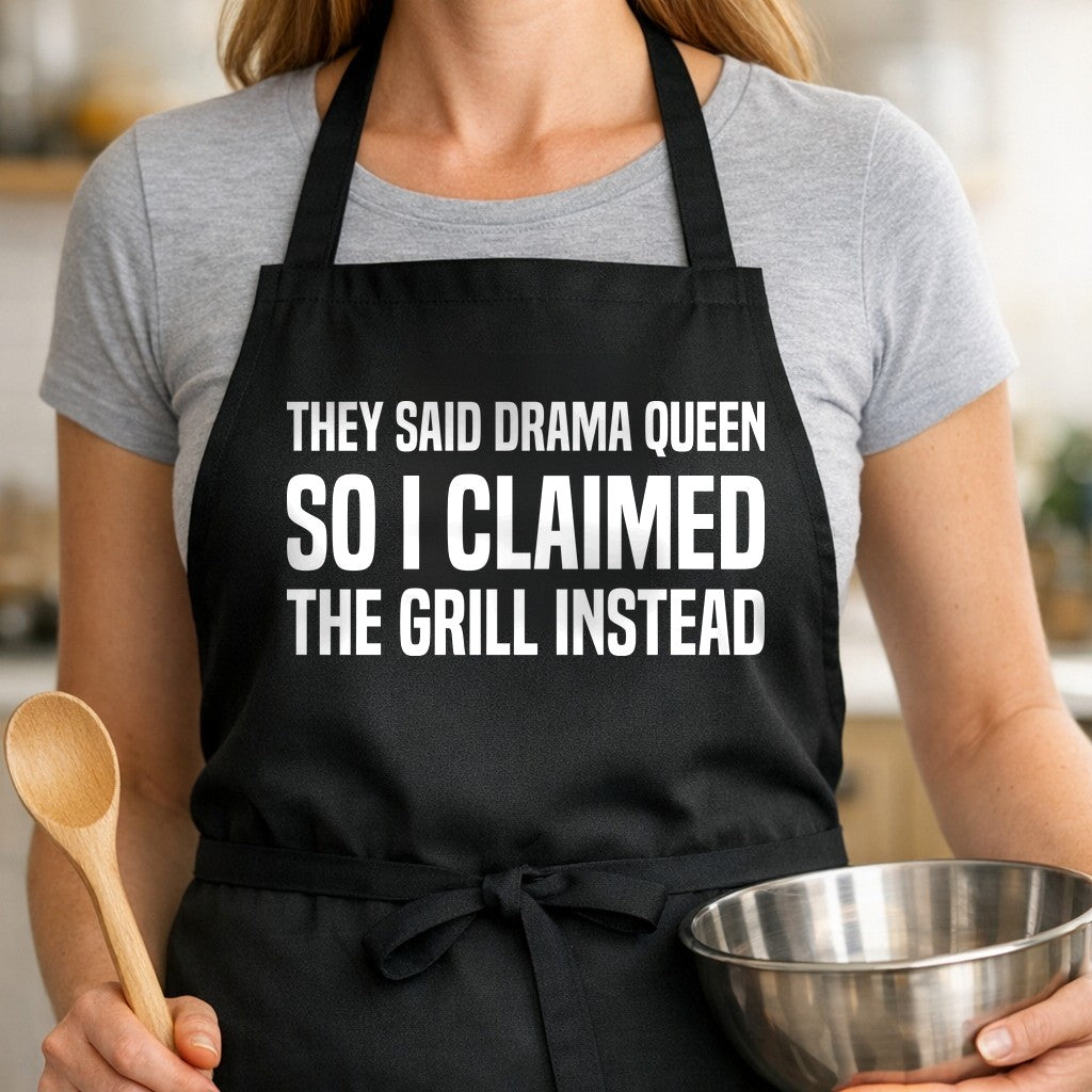 Black apron with large white block text reading 'They Said Drama Queen So I Claimed The Grill Instead' in a bold font.