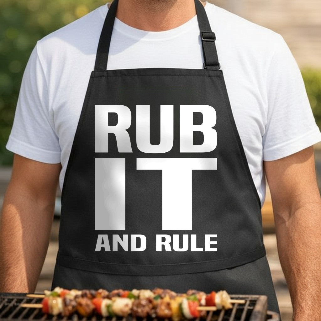 Black apron with large bold white text reading 'RUB IT AND RULE' in a modern block font on front