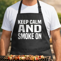 Black apron with large white block letters saying Keep Calm And Smoke On, simple bold text design on plain background.