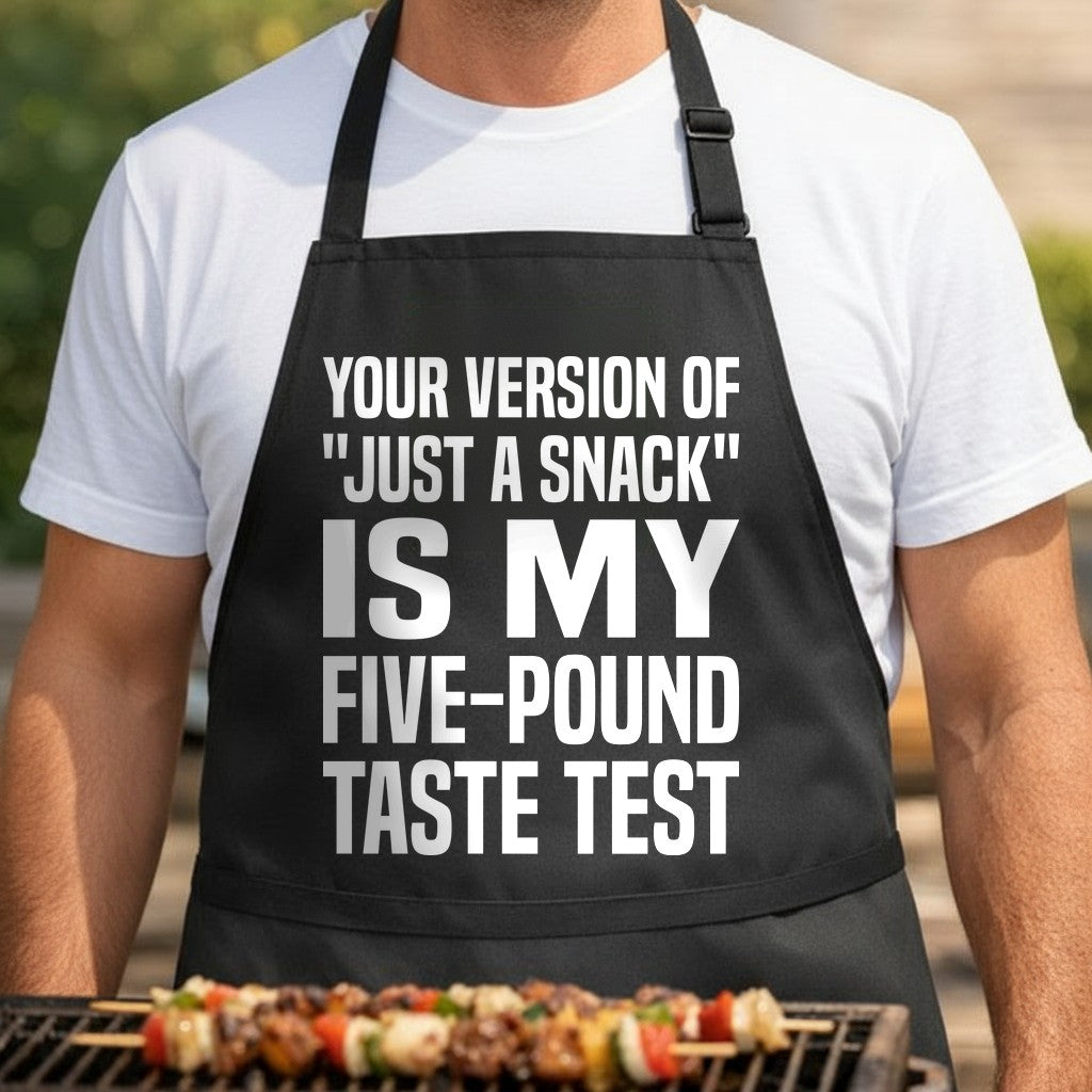 Black BBQ apron with bold white text reading Your Version of Just a Snack is My Five-Pound Taste Test in large uppercase letters