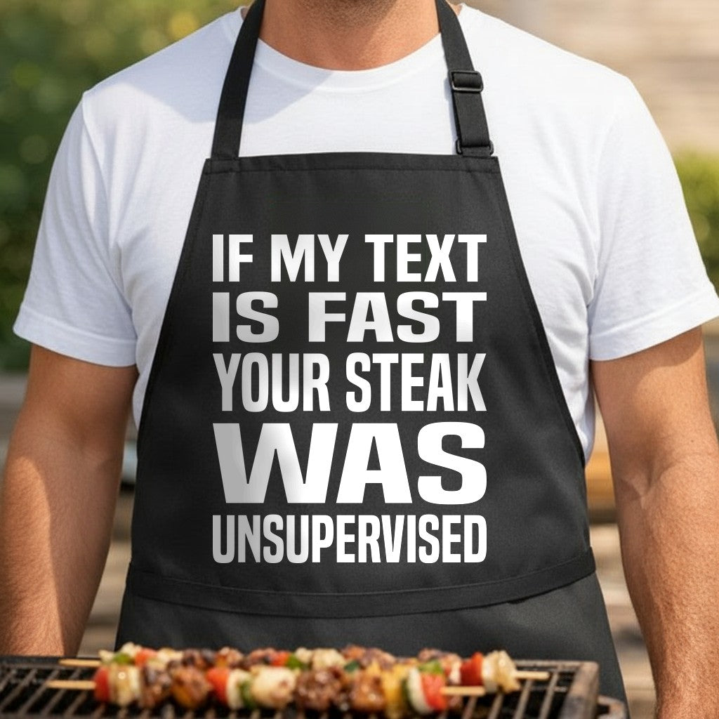 Black apron with large white bold text saying If My Text Is Fast Your Steak Was Unsupervised in simple typography