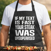 Black apron with large white bold text saying If My Text Is Fast Your Steak Was Unsupervised in simple typography