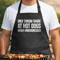 Black apron with large white text reading only throw shade at hot dogs when underdressed in bold font