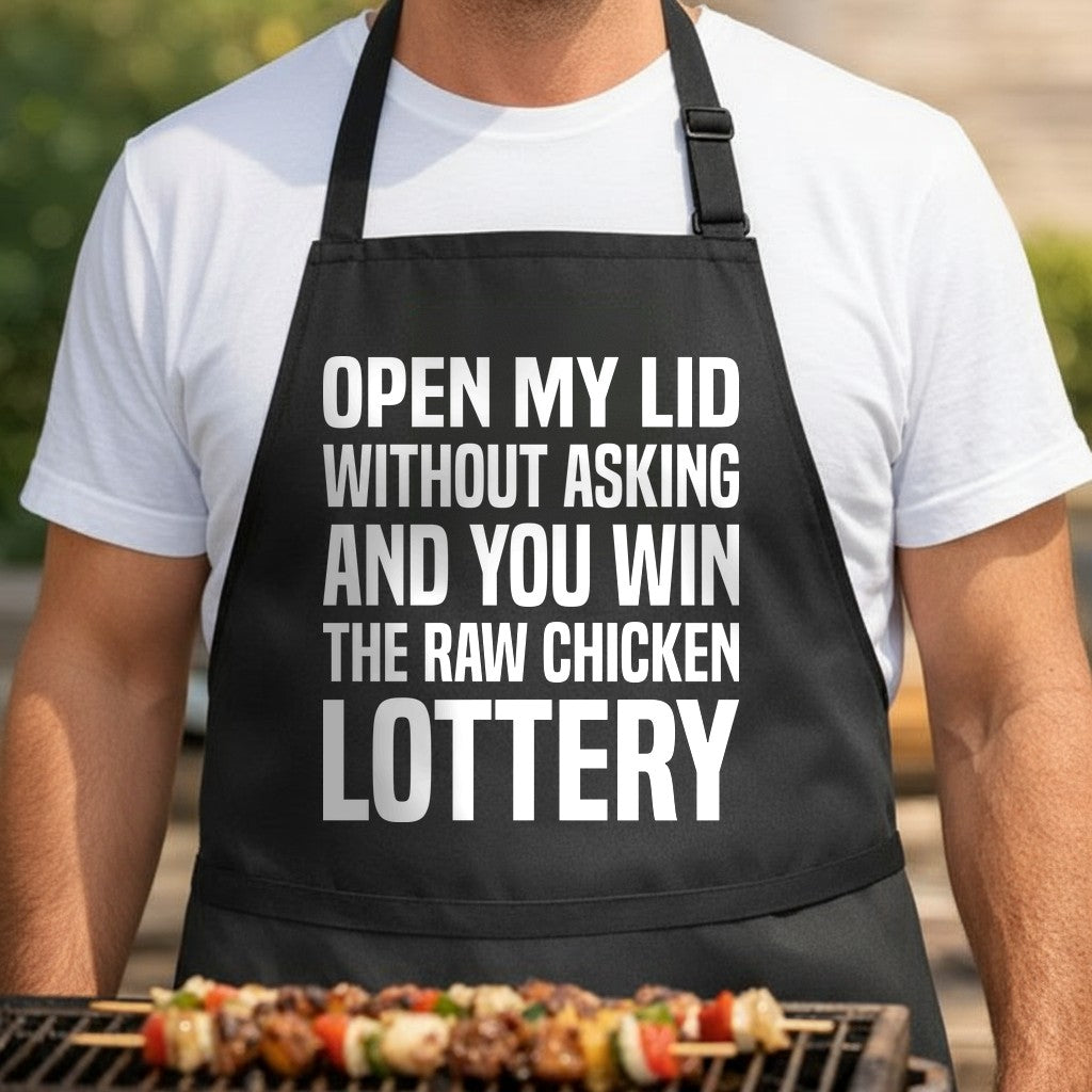 Black apron with large white text reading open my lid without asking and you win the raw chicken lottery in bold font