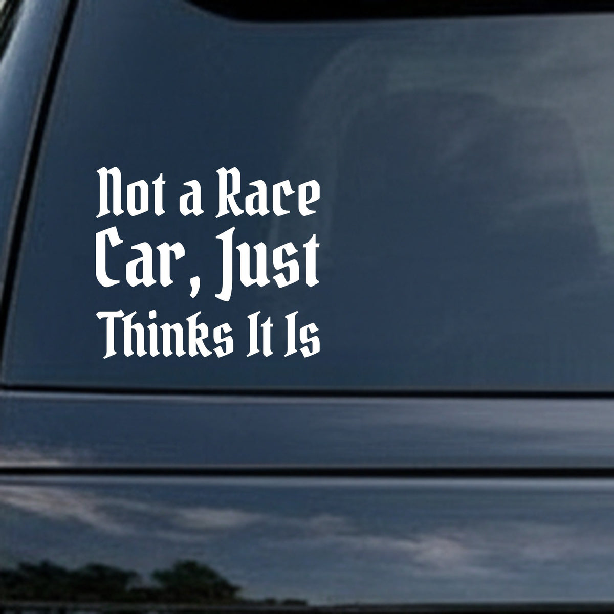 White gothic Old English style lettering saying Not a Race Car Just Thinks It Is on black background in a vinyl decal style