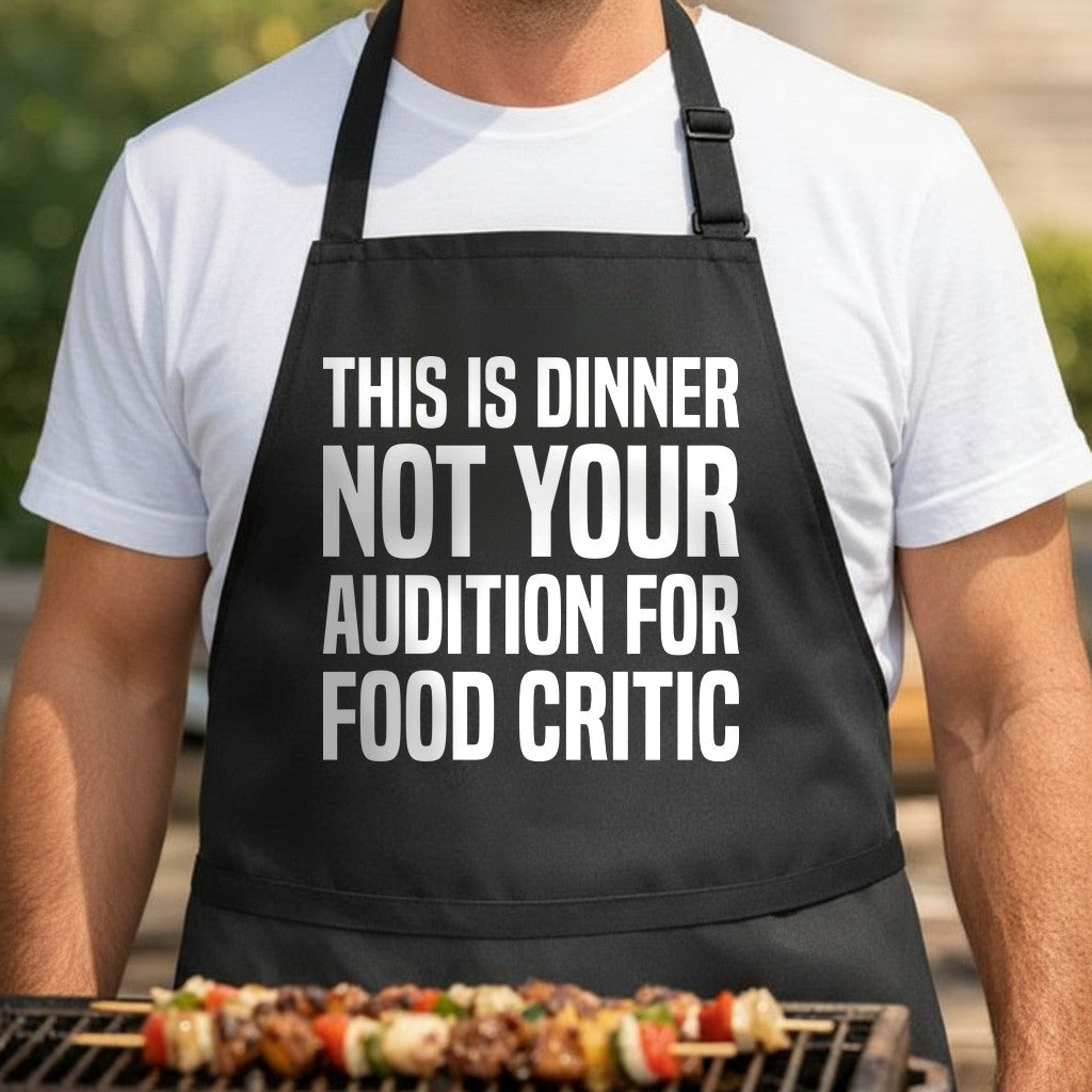 Black apron with large white bold text stating This Is Dinner Not Your Audition For Food Critic in a simple block font