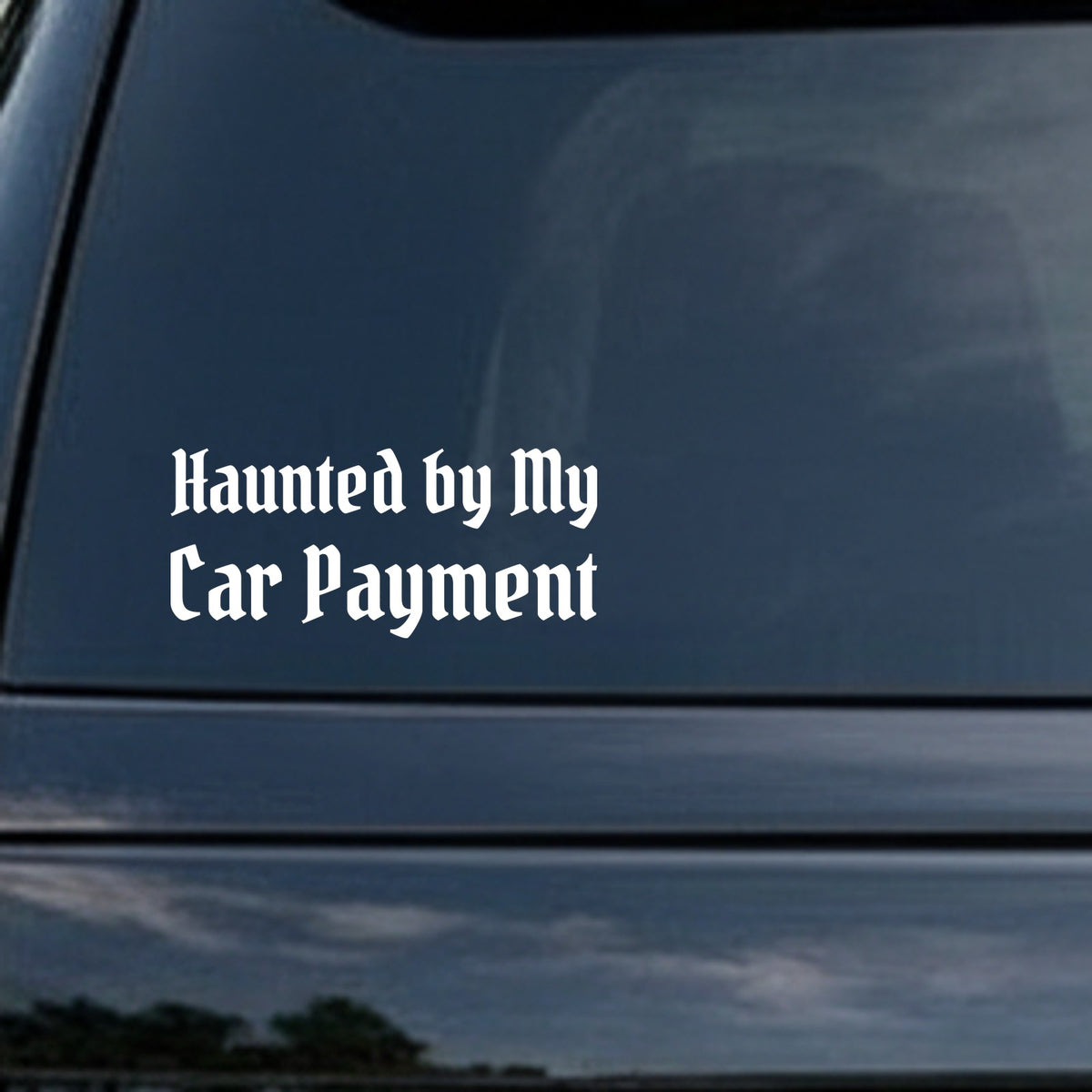 White gothic blackletter text reading 'Haunted by My Car Payment' on a solid black background in stylized old English font.