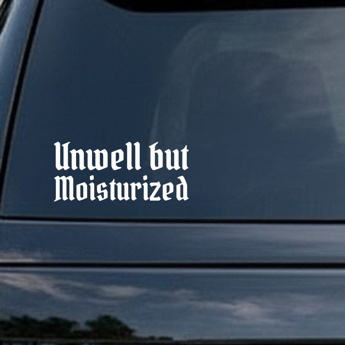 White gothic blackletter lettering spelling 'Unwell but Moisturized' on black background in Old English style font