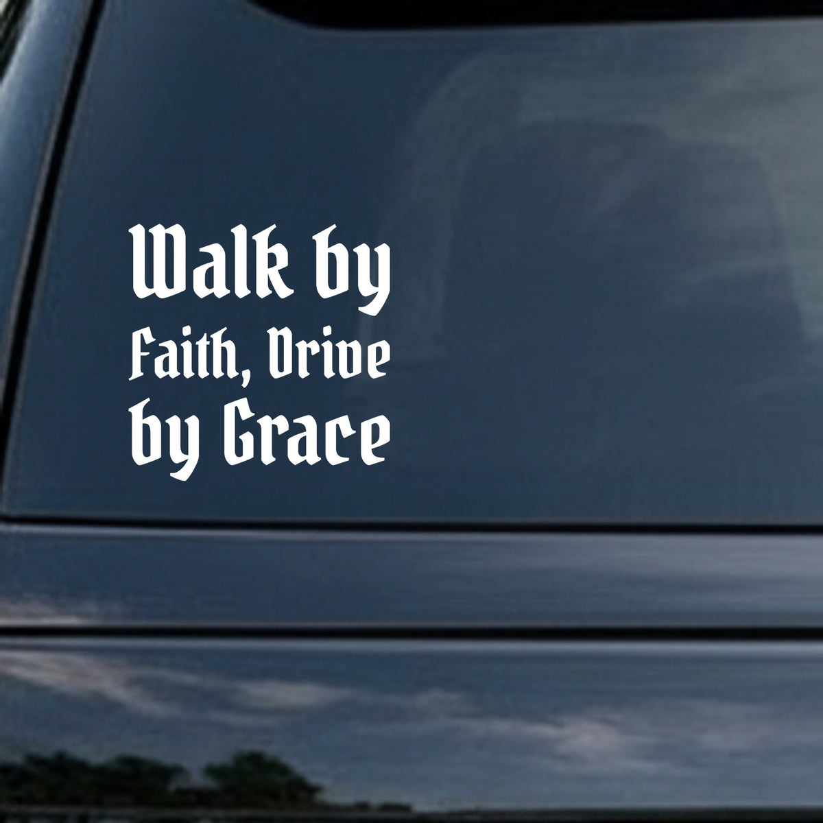 White lettering in gothic blackletter font saying Walk by Faith, Drive by Grace on a black background.