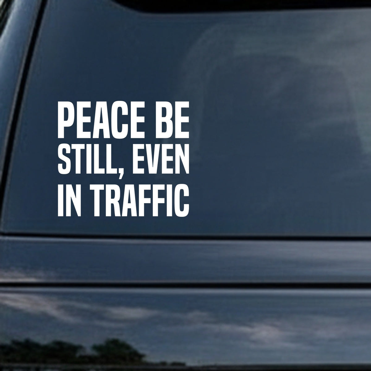 White vinyl decal with bold uppercase text saying Peace Be Still Even In Traffic on a solid black background in a clean modern font.