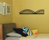 Black vinyl silhouette of Cologne's Hohenzollern Bridge showing its arching truss structure on a white background.