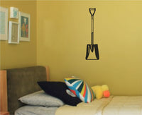 Black vinyl silhouette wall decal of a shovel with a long handle and D-shaped grip in a simple bold style