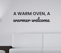 Black vinyl wall decal with the quote 'A warm oven, a warmer welcome' in a simple, modern font on a white background.