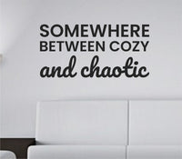Black vinyl wall decal with the quote 'Somewhere between cozy and chaotic' in a casual script style on a white background.