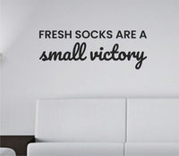 Black vinyl wall decal with the phrase 'Fresh socks are a small victory' in simple modern font on a white background.