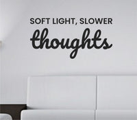 Simple black vinyl wall decal with the quote 'Soft light, slower thoughts.' in a smooth, modern font on a white background.