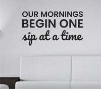 Black one-color vinyl wall decal with the quote Our mornings begin one sip at a time in a clean modern script style on a white background.