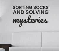 Black vinyl wall decal with the quote Sorting socks and solving mysteries in a clean modern font on a white background.