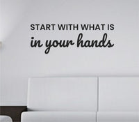 Black vinyl wall decal with the phrase Start with what is in your hands in a modern script and block lettering on a white background