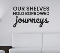 Black vinyl wall decal with the quote 'Our shelves hold borrowed journeys.' in a clean, modern script on a white background.