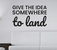 Black vinyl wall decal with the quote 'Give the idea somewhere to land' in elegant script font on a white background.