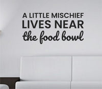 Black vinyl wall decal with the quote 'A little mischief lives near the food bowl' in playful script on a white background.