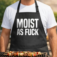 Black apron with large white block letters spelling 'MOIST AS FUCK' in bold uppercase font.