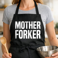 Black apron with large white text saying 'MOTHER FORKER' in bold block letters, simple and modern design.