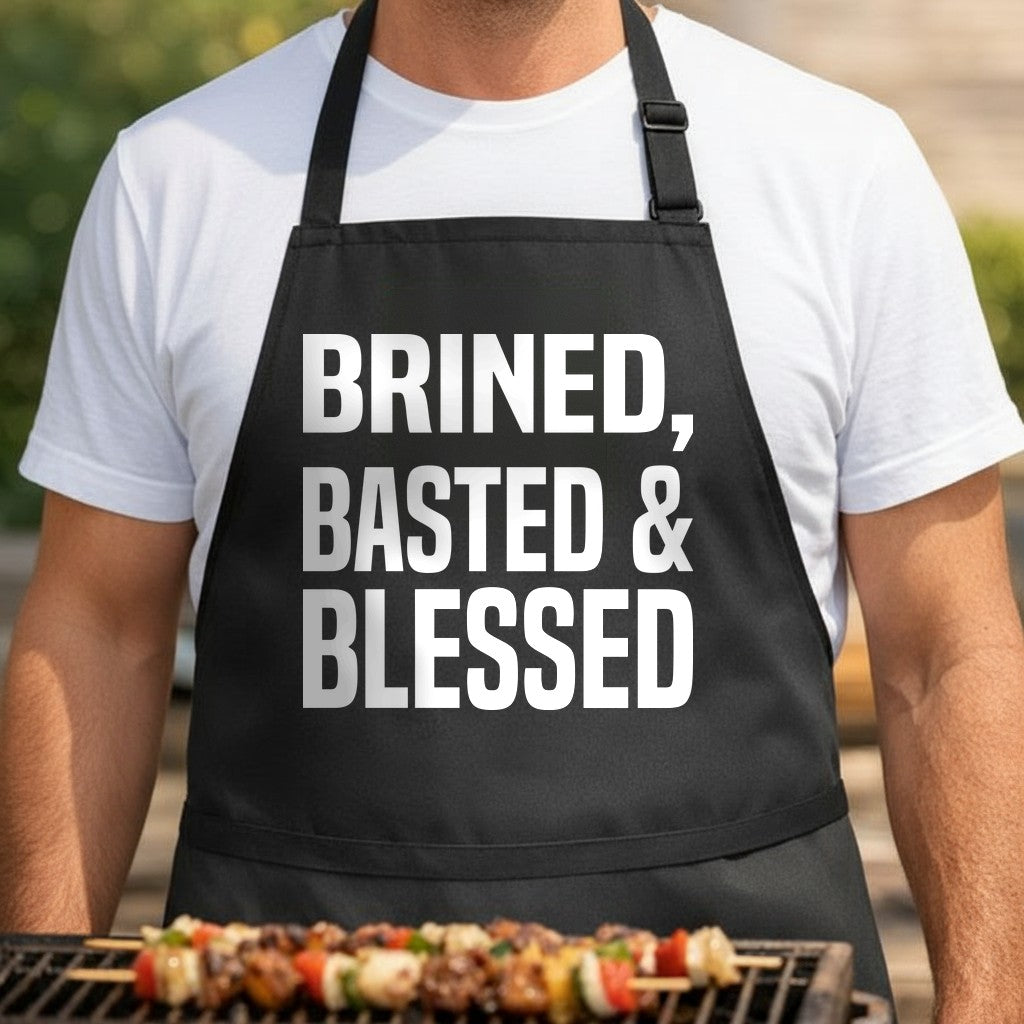 Black apron with large white bold text reading 'Brined, Basted & Blessed' in a simple block style.