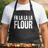 Black apron with large white text reading Fa La La La Flour in bold uppercase letters, minimalist holiday baking pun design.