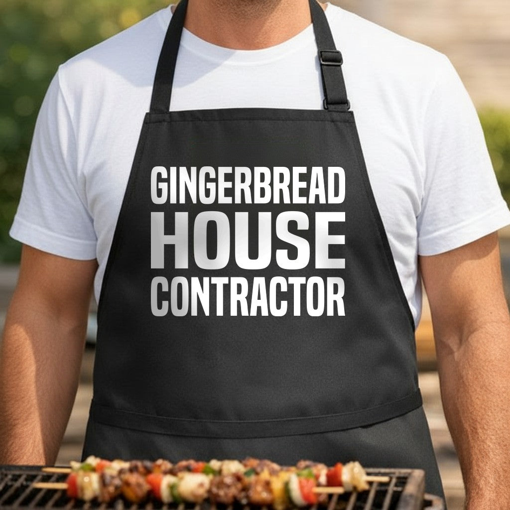 Black apron with large white text reading Gingerbread House Contractor in bold block letters, festive holiday kitchen wear.