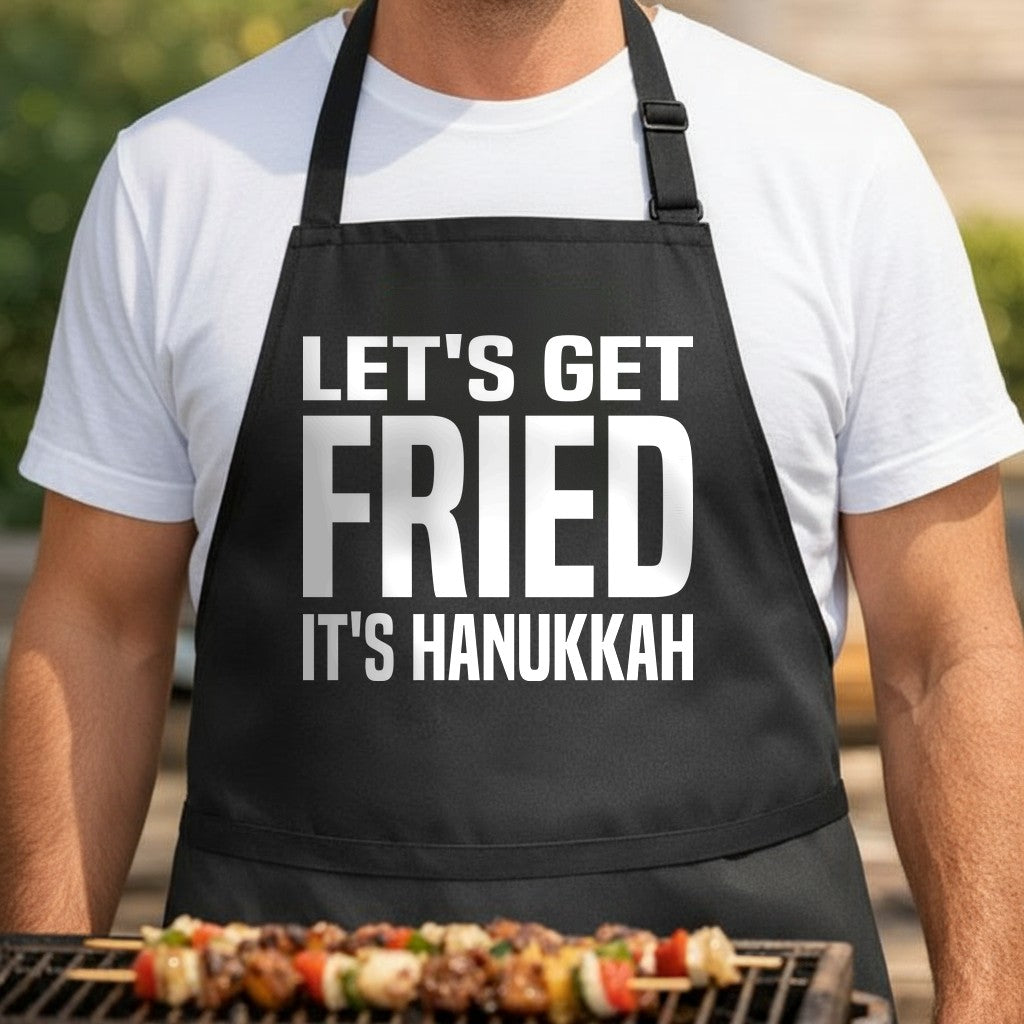 Black apron with large white text reading 'Let's Get Fried It's Hanukkah' in bold block letters