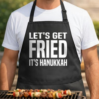 Black apron with large white text reading 'Let's Get Fried It's Hanukkah' in bold block letters