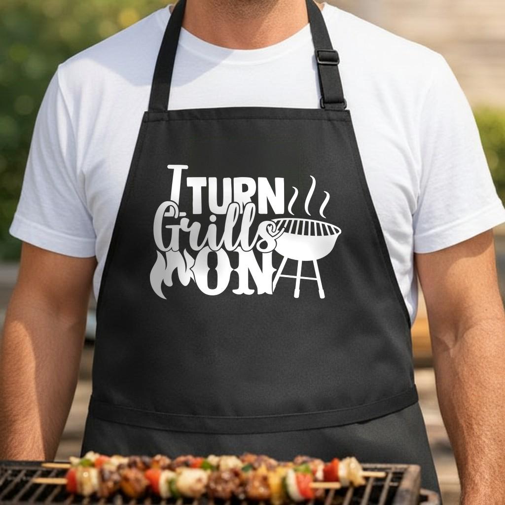 I Turn Grills On black BBQ apron, torso close-up: Black apron with bold white text 'I Turn Grills On' and a steaming round grill illustration in a playful font.