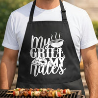 My Grill My Rules black BBQ apron, torso close-up: Black apron with white text saying ‘My Grill My Rules’ featuring a steaming grill and a steak illustration in bold graphic style.