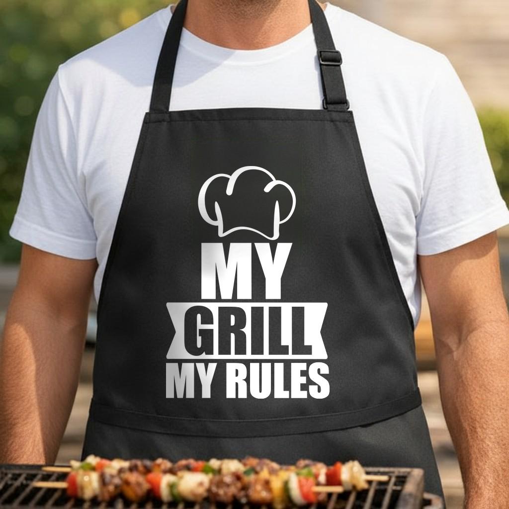 My Grill My Rules black BBQ apron, torso close-up: Black apron with white text saying 'MY GRILL MY RULES' and a white chef hat graphic above the text.