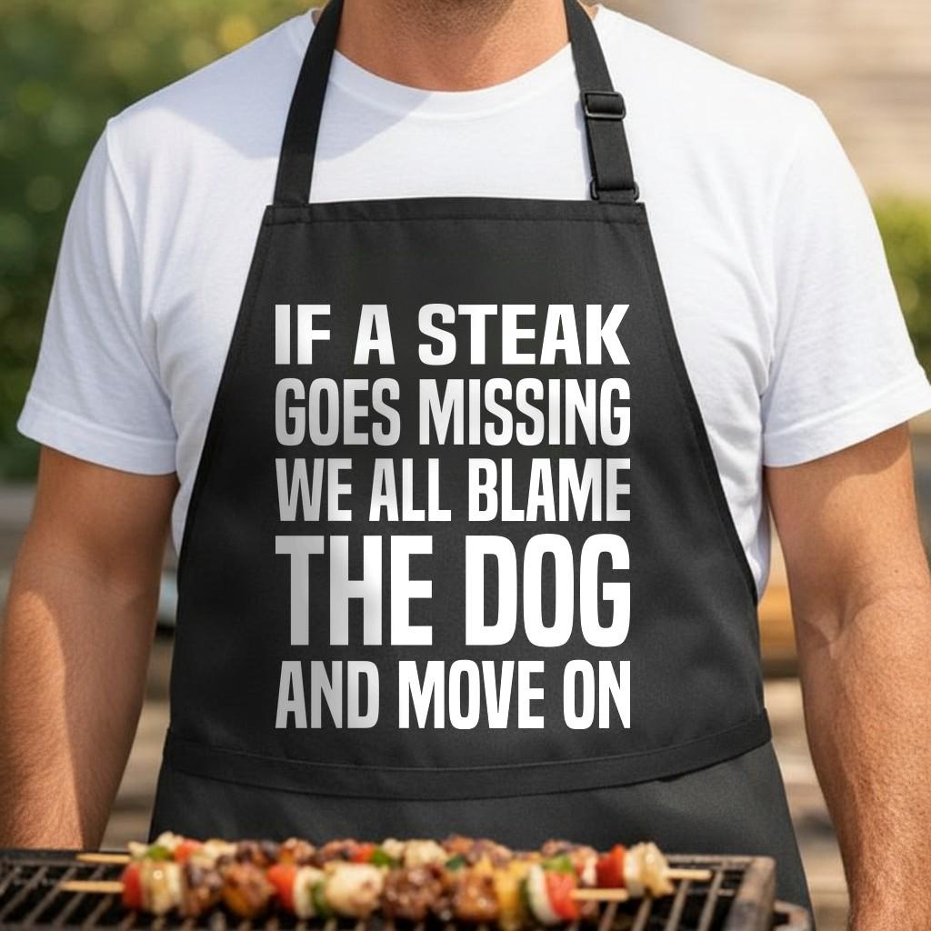 Blame The Dog black BBQ apron, torso close-up: Black apron with large bold white text stating If a steak goes missing we all blame the dog and move on in a simple font