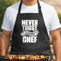 Never Trust a Skinny Chef black BBQ apron, torso close-up: Black apron with large white bold text reading Never Trust a Skinny Chef with a banner design around the word skinny