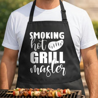 Smoking Hot Grill Master black BBQ apron, torso close-up: Black apron with white text reading 'Smoking Hot Grill Master' and a stylized steak graphic in bold and script fonts