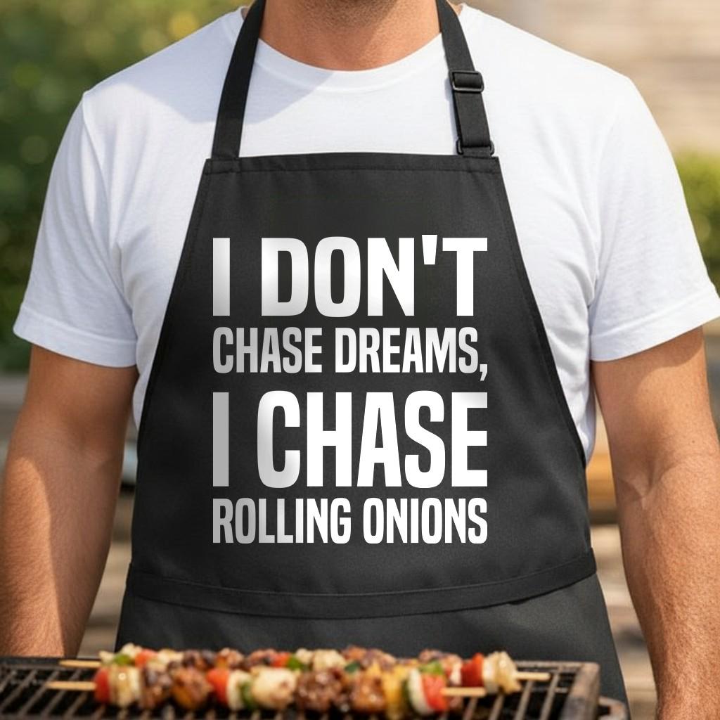 I Don't Chase Dreams, I Chase Rolling Onions black BBQ apron, torso close-up: Black apron with large white text reading I Don't Chase Dreams I Chase Rolling Onions in bold typography