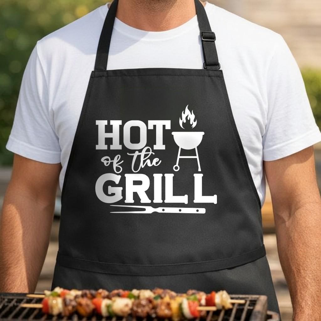 Hot off the Grill black BBQ apron, torso close-up: Black apron with white text saying Hot off the Grill, featuring a flaming charcoal grill and a fork graphic in a bold, clean style.
