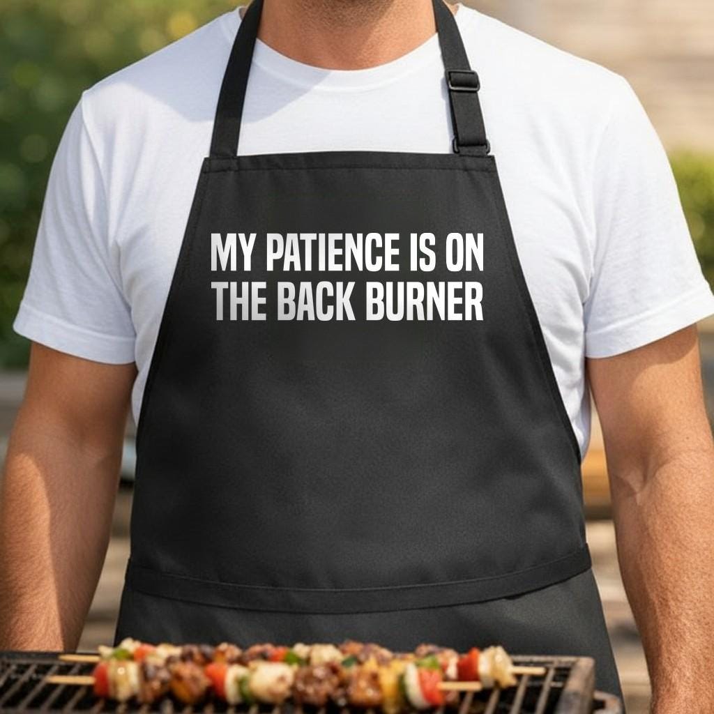 My Patience Is on the Back Burner black BBQ apron, torso close-up: Black apron with large white bold text saying My Patience Is on the Back Burner in uppercase letters