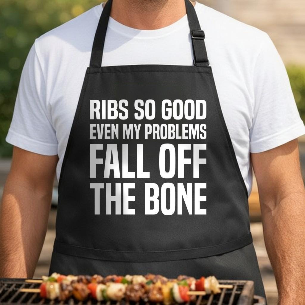 Bone-Deep Therapy black BBQ apron, torso close-up: Black apron with large white block text reading ribs so good even my problems fall off the bone in a bold uppercase font