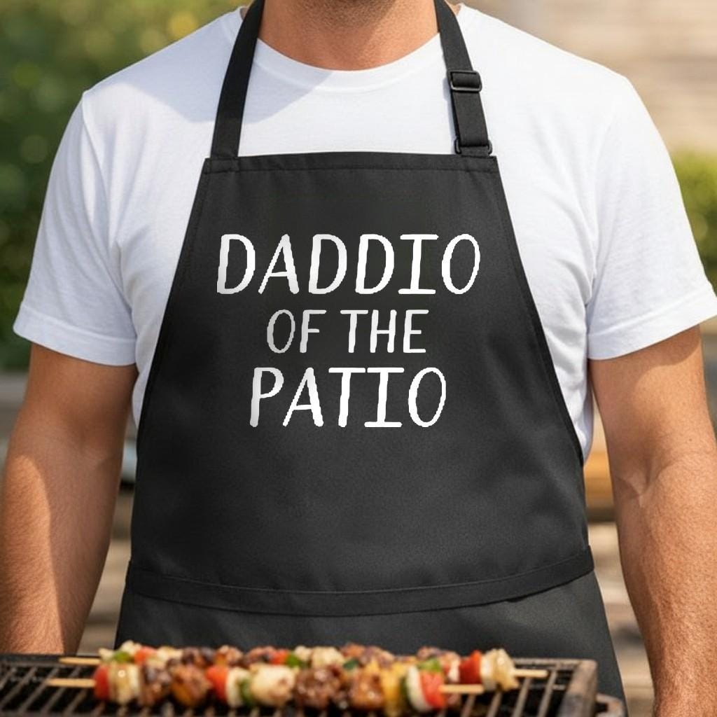 Daddio of the Patio black BBQ apron, torso close-up: Black BBQ apron with white text saying 'Daddio of the Patio' in a bold hand-drawn style font
