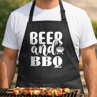 Beer and BBQ black BBQ apron, torso close-up: Black apron with white bold text reading 'Beer and BBQ' and a small graphic of a steaming grill.