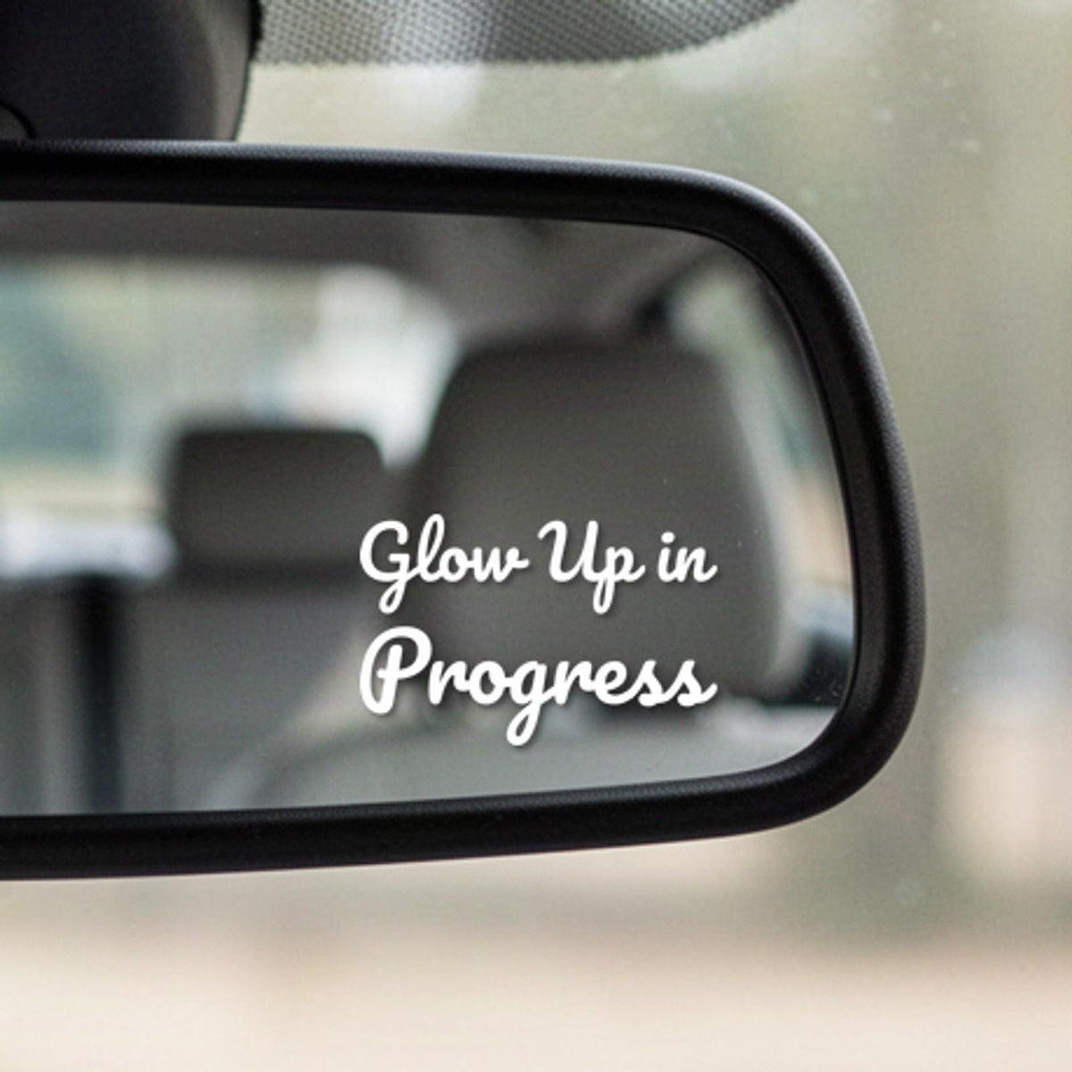 Close-up of the Glow Up In Progress white vinyl decal in the corner of a rear-view mirror