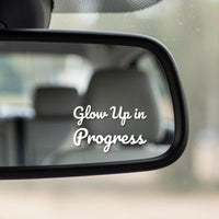 Close-up of the Glow Up In Progress white vinyl decal in the corner of a rear-view mirror